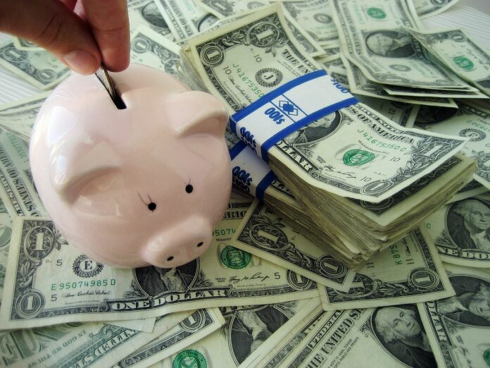 1280px-Putting_money_into_a_piggybank